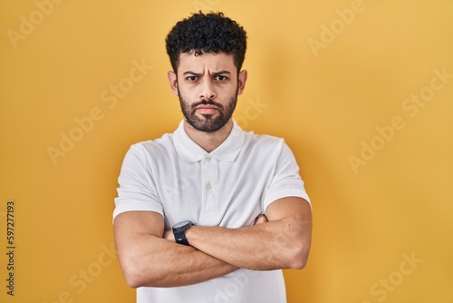 Arab man standing over yellow background skeptic and nervous, disapproving expression on face with crossed arms. negative person.