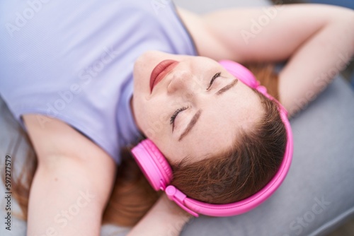 Young redhead woman listening to music lying on sofa at home