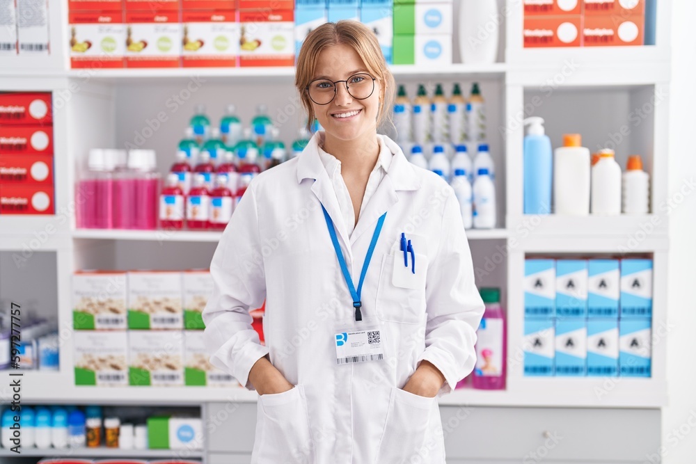 Young blonde girl pharmacist smiling confident standing at pharmacy