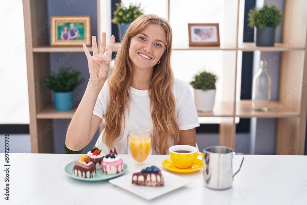 Young caucasian woman eating pastries t for breakfast showing and pointing up with fingers number four while smiling confident and happy.