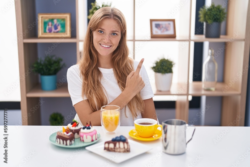 Young caucasian woman eating pastries t for breakfast cheerful with a smile of face pointing with hand and finger up to the side with happy and natural expression on face