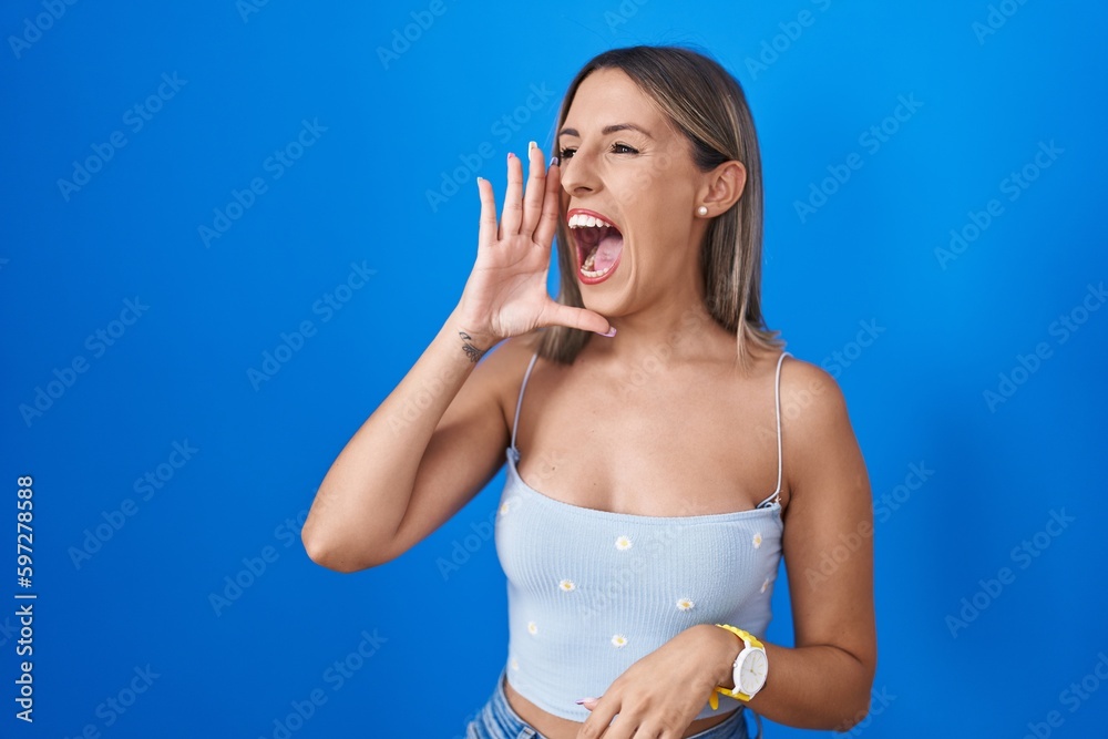 Young woman standing over blue background shouting and screaming loud to side with hand on mouth. communication concept. Young woman standing over blue background shouting and screaming loud to side with hand on mouth. communication concept.
