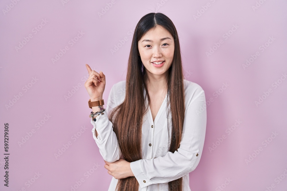 Chinese young woman standing over pink background with a big smile on face, pointing with hand finger to the side looking at the camera. Chinese young woman standing over pink background with a big smile on face, pointing with hand finger to the side looking at the camera.