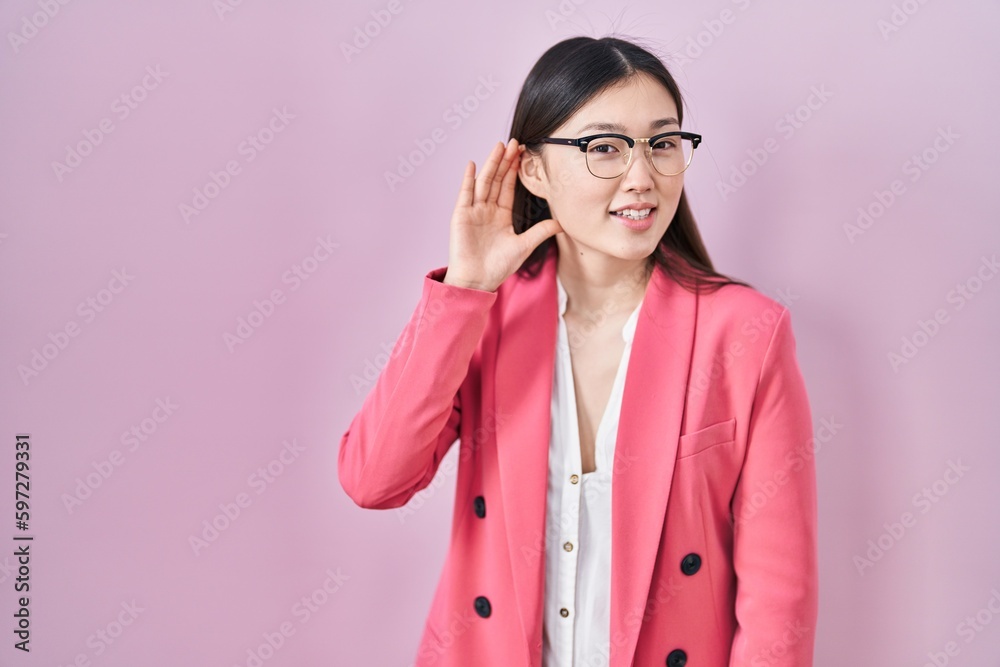Chinese business young woman wearing glasses smiling with hand over ear listening an hearing to rumor or gossip. deafness concept.
