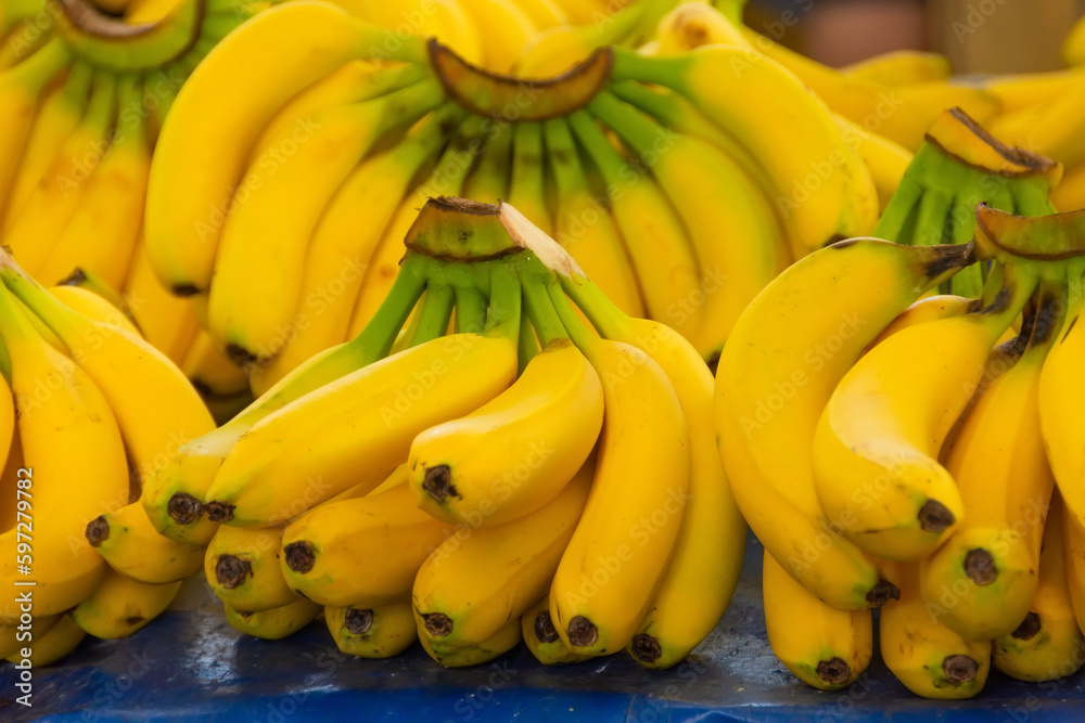Yellow ripe bananas lie on a market stall with other fruits in the background.