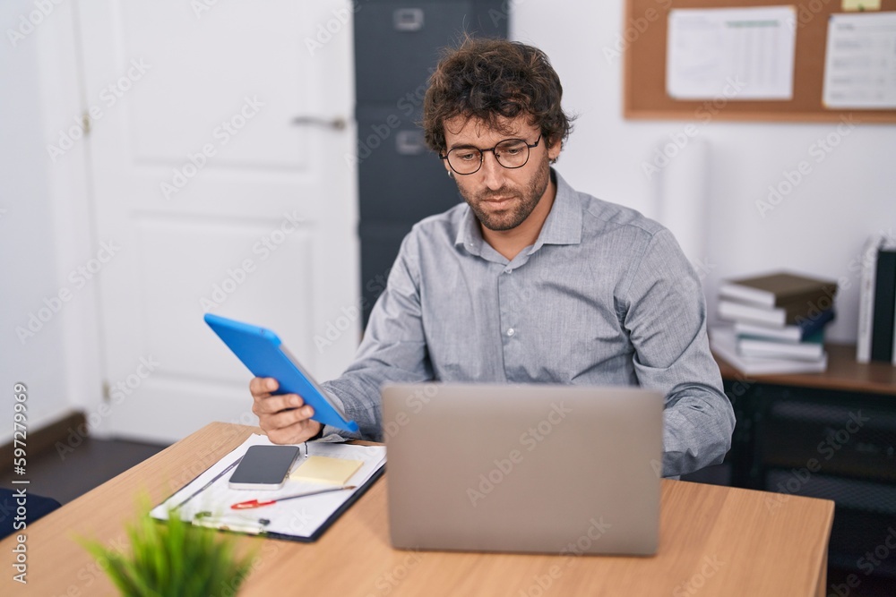 Young hispanic man business worker using touchpad and laptop at office Young hispanic man business worker using touchpad and laptop at office