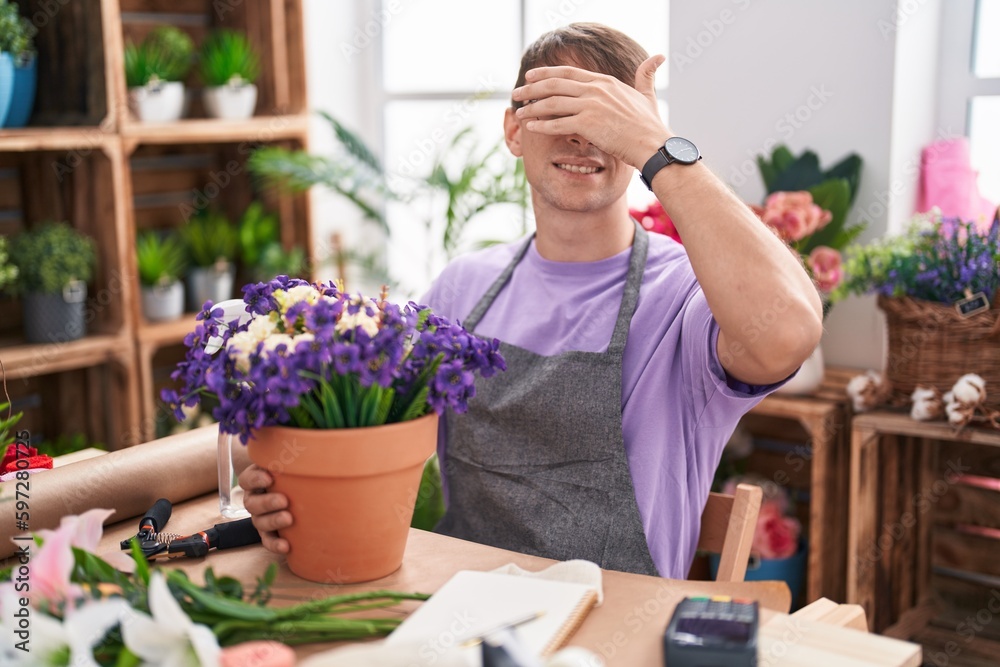 Caucasian blond man working at florist shop smiling and laughing with hand on face covering eyes for surprise. blind concept. Caucasian blond man working at florist shop smiling and laughing with hand on face covering eyes for surprise. blind concept.