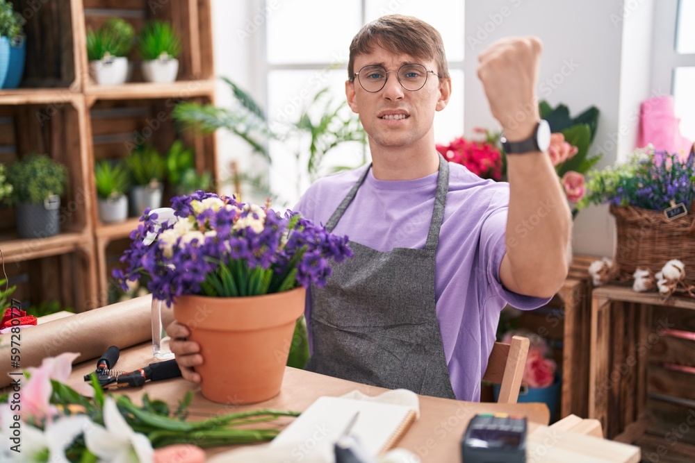 Caucasian blond man working at florist shop angry and mad raising fist frustrated and furious while shouting with anger. rage and aggressive concept.