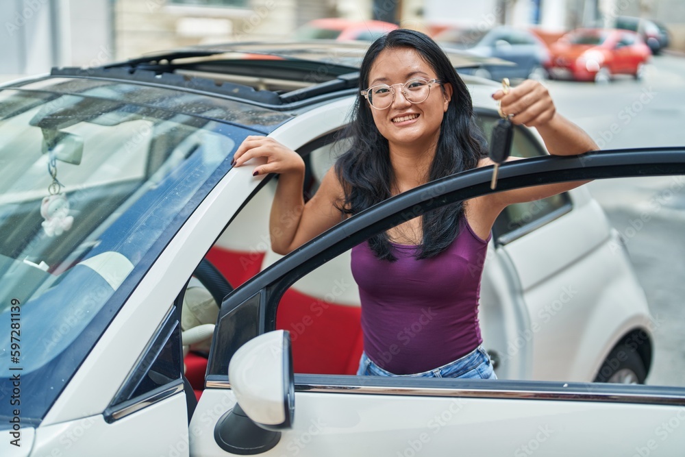 Young chinese woman smiling confident holding key of new car at street