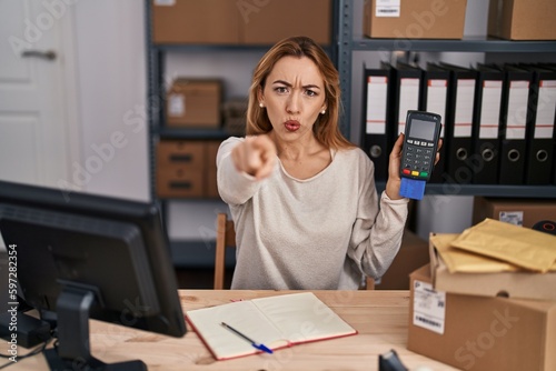 Hispanic woman working at small business ecommerce holding credit card and dataphone pointing with finger to the camera and to you, confident gesture looking serious