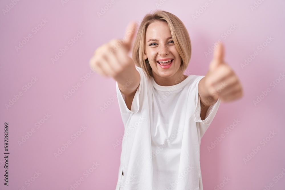 Young caucasian woman standing over pink background approving doing positive gesture with hand, thumbs up smiling and happy for success. winner gesture. Young caucasian woman standing over pink background approving doing positive gesture with hand, thumbs up smiling and happy for success. winner gesture.