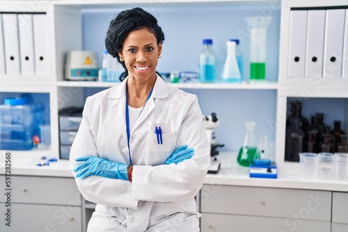 African american woman wearing scientist uniform with arms crossed gesture at laboratory