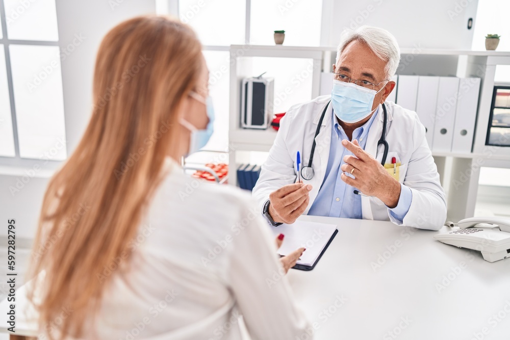 Middle age man and woman doctor and patient wearing medical mask having consultation at clinic
