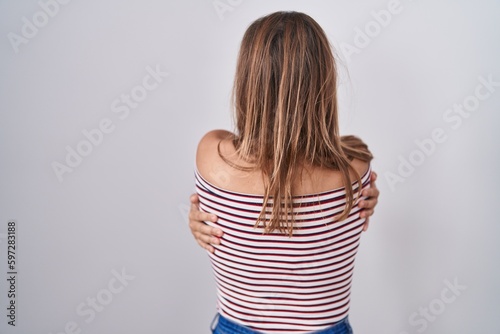 Young hispanic woman standing over isolated background hugging oneself happy and positive from backwards. self love and self care photo
