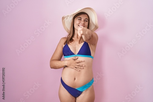 Young hispanic woman wearing bikini over pink background laughing at you, pointing finger to the camera with hand over body, shame expression