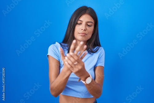 Brunette young woman standing over blue background suffering pain on hands and fingers, arthritis inflammation © Krakenimages.com