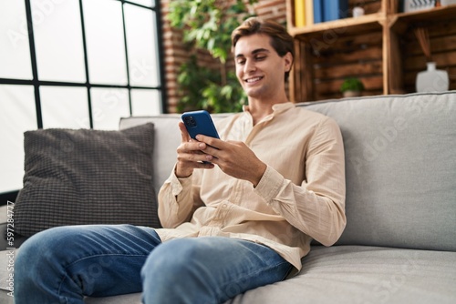 Young caucasian man using smartphone sitting on sofa at home