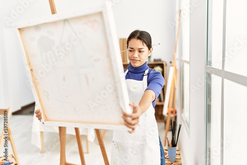 Young latin woman looking canvas draw at art studio