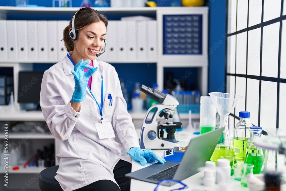 Hispanic woman working at scientist laboratory doing ok sign with fingers, smiling friendly gesturing excellent symbol