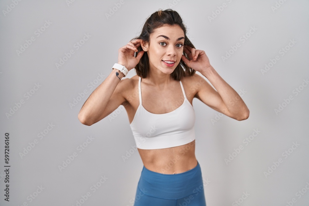 Hispanic woman wearing sportswear over isolated background smiling pulling ears with fingers, funny gesture. audition problem Hispanic woman wearing sportswear over isolated background smiling pulling ears with fingers, funny gesture. audition problem