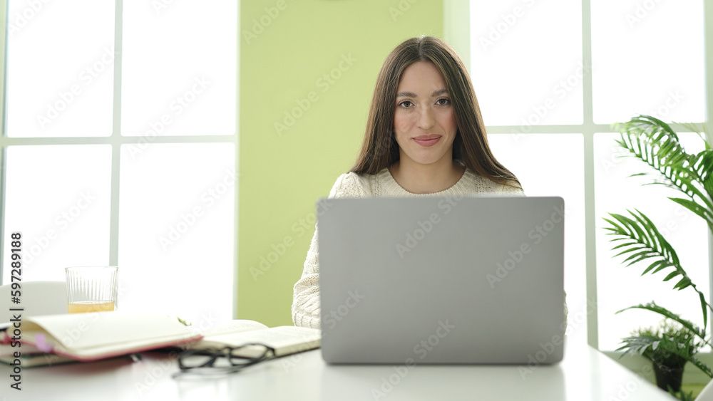 Fototapeta premium Young beautiful hispanic woman student smiling confident using laptop studying at home