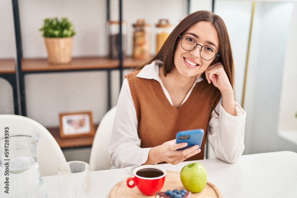 Young beautiful hispanic woman having breakfast using smartphone at home