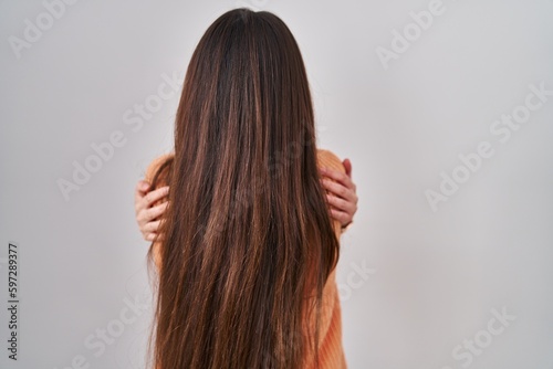 Young brunette woman standing over white background hugging oneself happy and positive from backwards. self love and self care