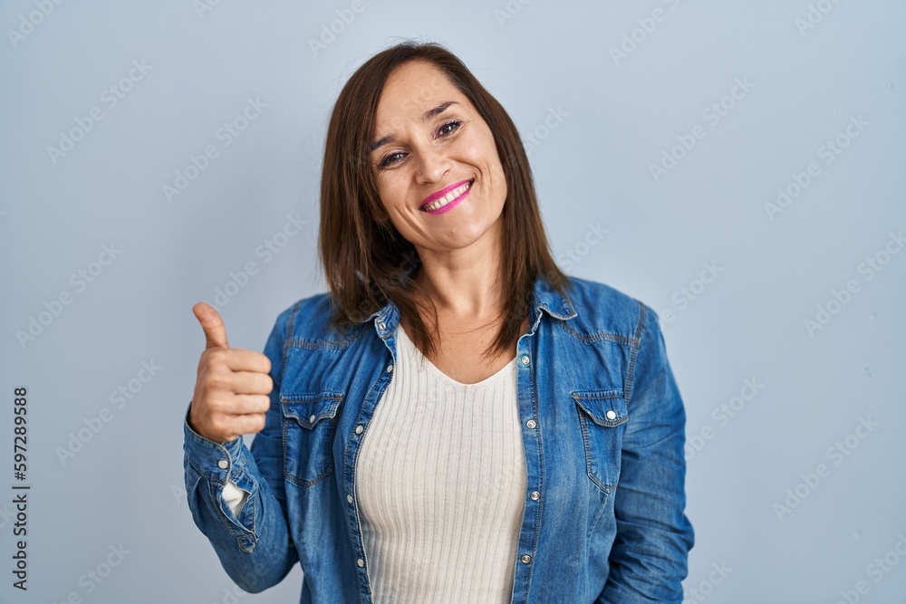 Middle age brunette woman wearing casual denim jacket over isolated background doing happy thumbs up gesture with hand. approving expression looking at the camera showing success. Middle age brunette woman wearing casual denim jacket over isolated background doing happy thumbs up gesture with hand. approving expression looking at the camera showing success.