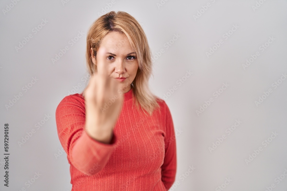 Blonde woman standing over isolated background showing middle finger, impolite and rude fuck off expression Blonde woman standing over isolated background showing middle finger, impolite and rude fuck off expression