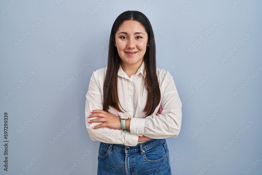 Young latin woman standing over blue background happy face smiling with crossed arms looking at the camera. positive person.