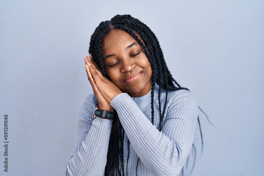 African american woman standing over blue background sleeping tired dreaming and posing with hands together while smiling with closed eyes. African american woman standing over blue background sleeping tired dreaming and posing with hands together while smiling with closed eyes.