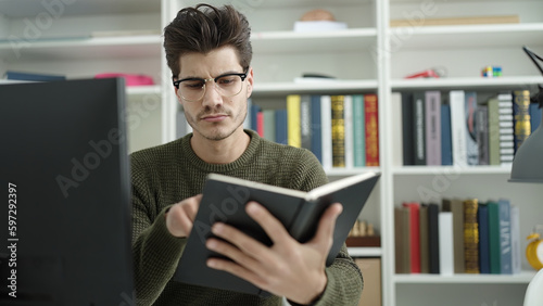 Young hispanic man student reading book studying at library university