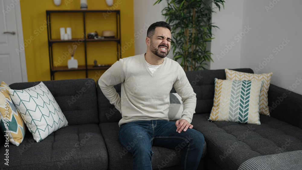 Young hispanic man suffering for backache sitting on sofa at home