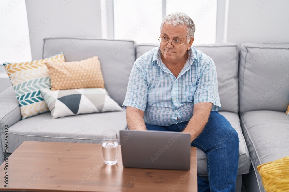 Middle age grey-haired man using laptop sitting on sofa at home Middle age grey-haired man using laptop sitting on sofa at home