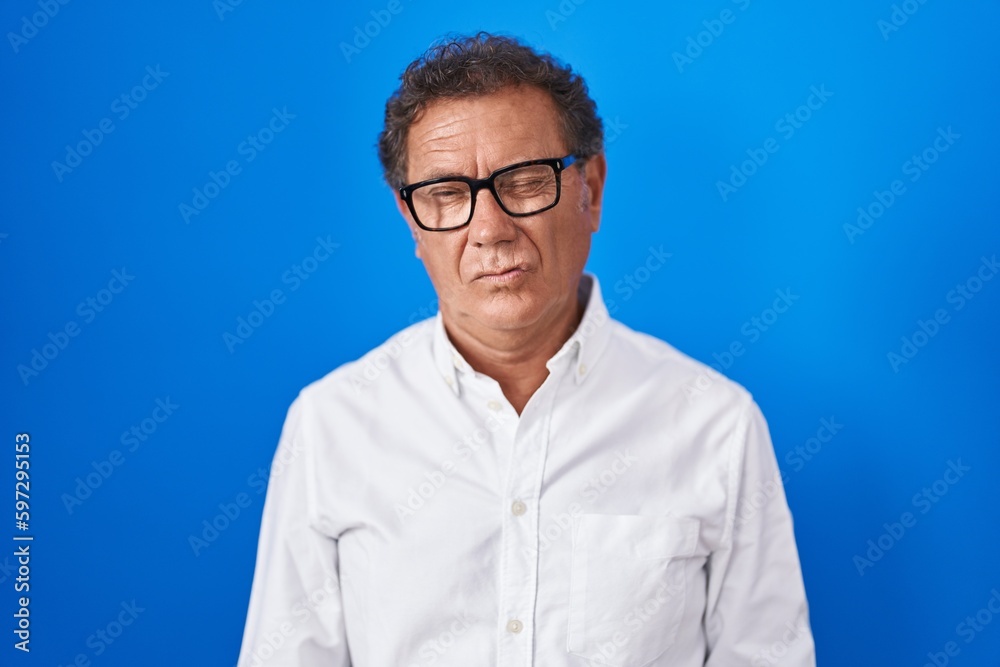 Middle age hispanic man standing over blue background winking looking at the camera with sexy expression, cheerful and happy face. Middle age hispanic man standing over blue background winking looking at the camera with sexy expression, cheerful and happy face.