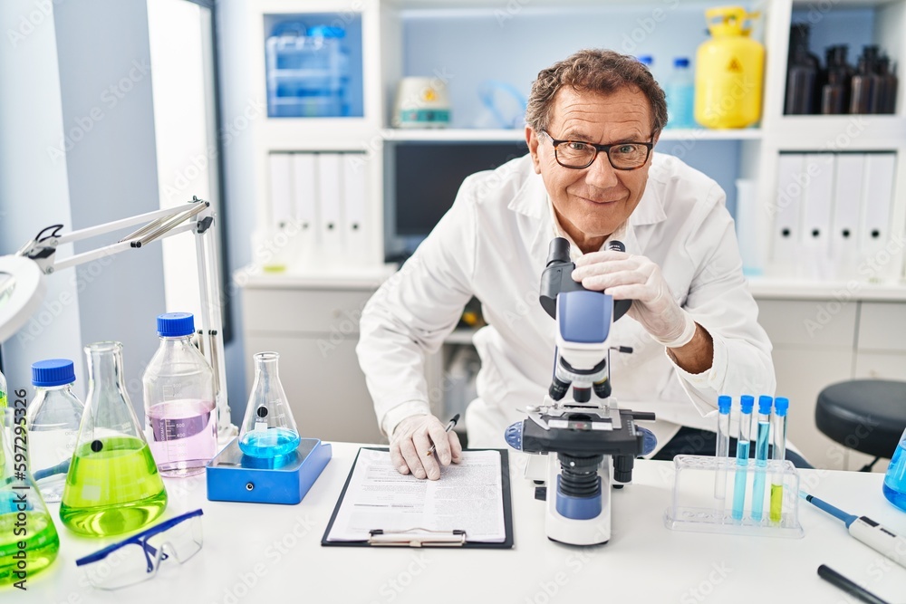 Middle age man wearing scientist uniform using microscope at laboratory Middle age man wearing scientist uniform using microscope at laboratory
