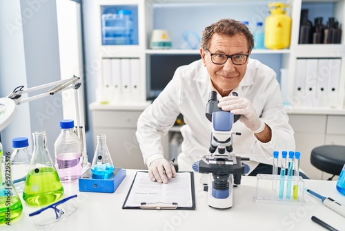 Middle age man wearing scientist uniform using microscope at laboratory