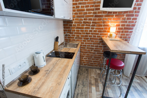 Bright kitchen with wooden countertop. Home decor room in the style of a loft. Morning light outside the window. Bar counter at the brick wall. TV on the background of brick walls.