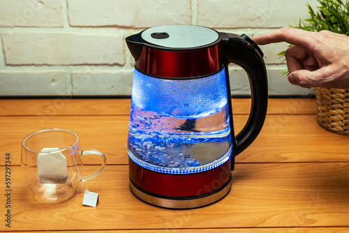 man turns off the heating button of a modern glass electric kettle photo