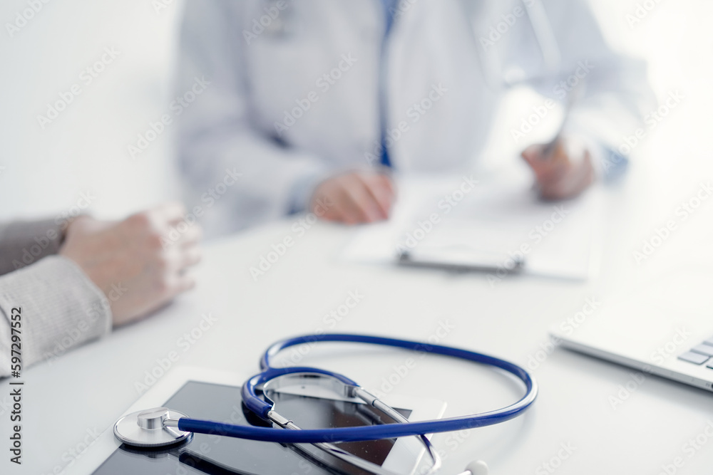 Stethoscope lying on the tablet computer in front of a doctor and patient at the background . Medicine, healthcare, reasuring hands concept. Stethoscope lying on the tablet computer in front of a doctor and patient at the background . Medicine, healthcare, reasuring hands concept.