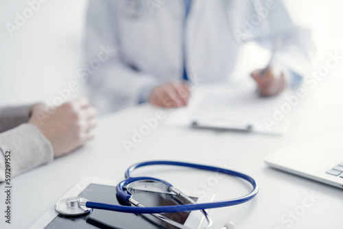 Stethoscope lying on the tablet computer in front of a doctor and patient at the background . Medicine, healthcare, reasuring hands concept.