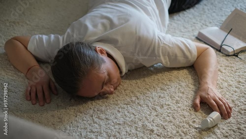 A woman lies unconscious on the floor with scattered pills next to her.