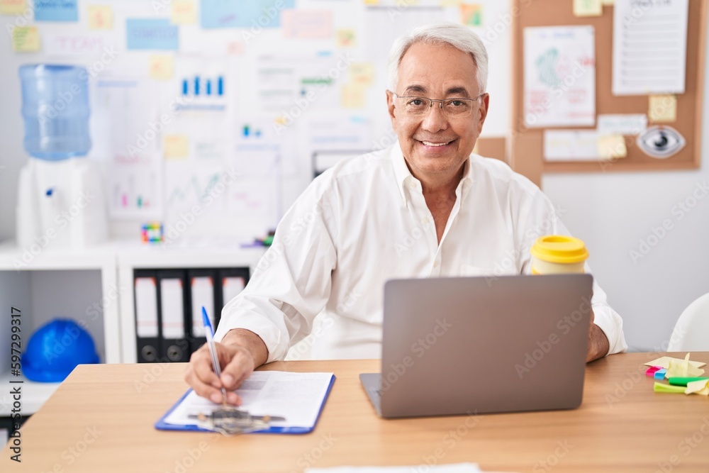 Middle age grey-haired man business worker using laptop writing on document at office Middle age grey-haired man business worker using laptop writing on document at office