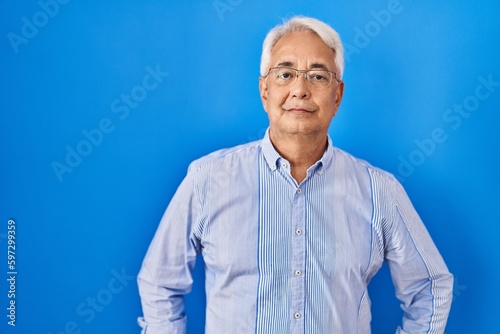Hispanic senior man wearing glasses relaxed with serious expression on face. simple and natural looking at the camera.