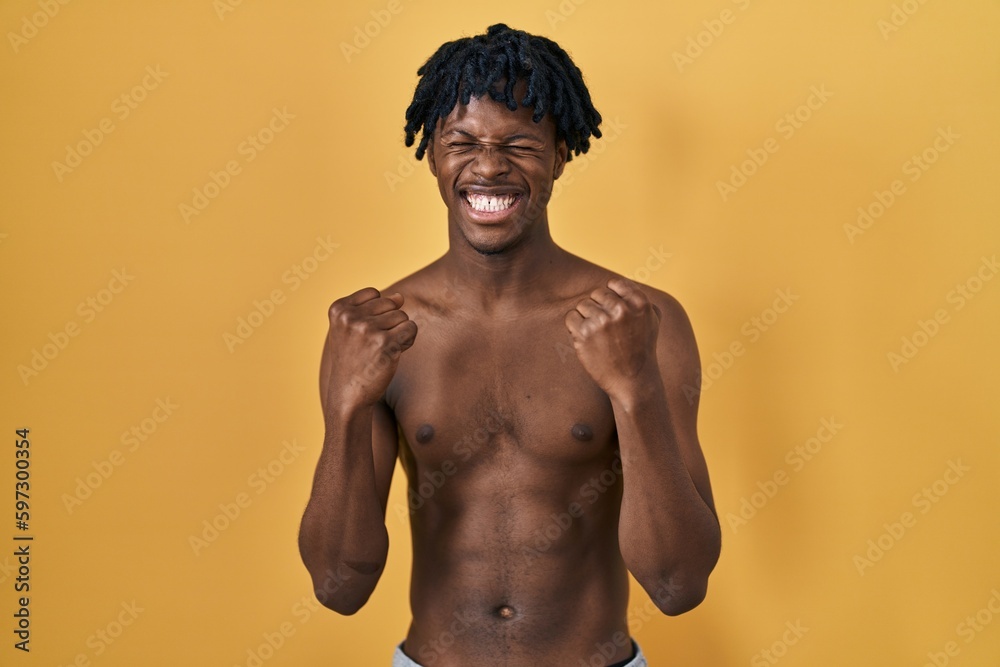 Fototapeta premium Young african man with dreadlocks standing shirtless excited for success with arms raised and eyes closed celebrating victory smiling. winner concept.