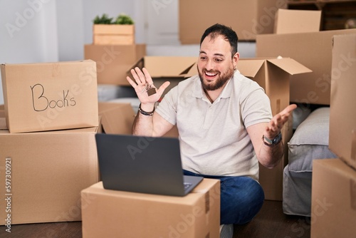 Plus size hispanic man with beard moving to a new home doing video call celebrating achievement with happy smile and winner expression with raised hand
