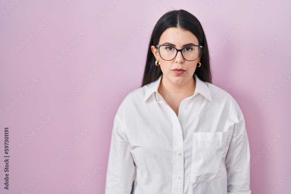 Young brunette woman standing over pink background relaxed with serious expression on face. simple and natural looking at the camera.