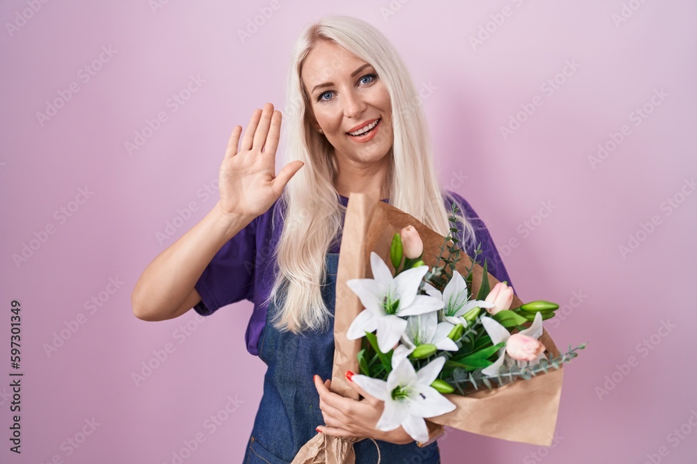Caucasian woman holding bouquet of white flowers waiving saying hello happy and smiling, friendly welcome gesture
