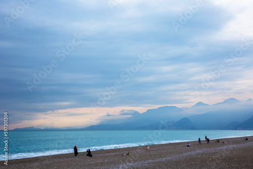 Storm in the Mediterranean Sea. Beautiful rocky shore with rolling waves and walking people. Turkiye, Antalya.
