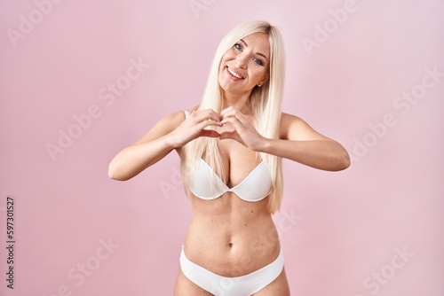 Caucasian woman wearing lingerie over pink background smiling in love doing heart symbol shape with hands. romantic concept.